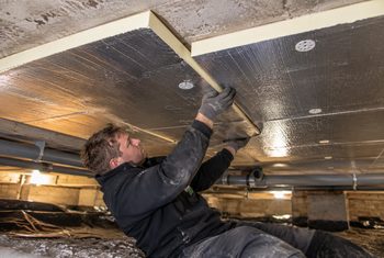Betonnen vloer isoleren met PIR-isolatieplaten Monteur bevestigt PIR-isolatieplaten tegen de onderzijde van een betonnen vloer in een kruipruimte