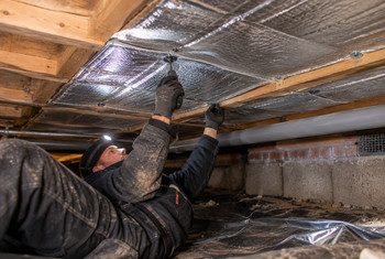 Houten vloer isoleren met reflecterende thermokussens Monteur bevestigt reflecterende thermokussens tegen de onderzijde van een houten vloer in een kruipruimte