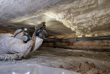 Monteur brengt gespoten PUR-schuim aan tegen de onderzijde van een vloer in een kruipruimte