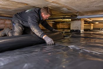 Kruipruimte voorzien van vochtwerende bodemfolie Monteur brengt vochtwerende bodemfolie aan op de bodem van een kruipruimte om optrekkend vocht te beperken